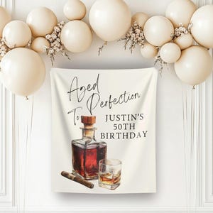 Può includere: Banner color crema con la scritta "Aged to Perfection" e "Justin's 50th Birthday". Il banner presenta un'illustrazione ad acquerello di una bottiglia di whisky, un bicchiere di whisky e un sigaro. Decorato con palloncini color crema.