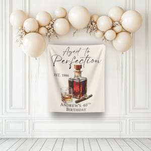 Può includere: Uno striscione rettangolare in tessuto con un'illustrazione ad acquerello di un decanter in vetro, un bicchiere di liquido ambrato e un sigaro. Il testo recita Aged to Perfection, EST. 1986 e ANDREW'S 40TH BIRTHDAY. Lo striscione è decorato con palloncini color crema.