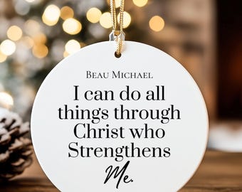 May include: A white, round Christmas ornament with gold hanging string. The ornament has the text "I can do all things through Christ who Strengthens Me. Philippians 4:13". The background includes a fireplace and Christmas lights.