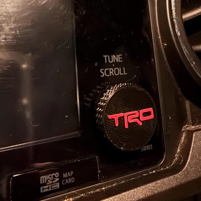 May include: Close-up of a black control knob with the red letters "TRD" on it. The knob is for tuning and scrolling. The text "TUNE SCROLL" is above the knob. The image also shows a "micro SD HC" card slot.