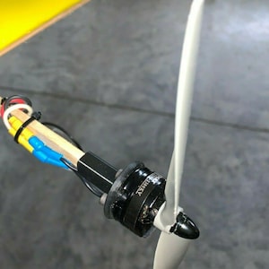 Puede incluir: Primer plano de un pequeño motor eléctrico negro con una hélice gris unida. El motor tiene el texto "2200KV" impreso en él.