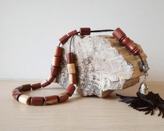 May include: A wooden prayer beads necklace with a brown tassel and a silver charm. The beads are made of two different types of wood, one light brown and one dark brown.