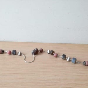 Può includere: Una collana a catena d'argento con una varietà di perline, tra cui rosa, grigio e bianco. Le perline sono realizzate con diversi materiali, tra cui pietra e vetro.