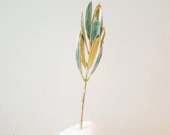 May include: A small gold and green metal sculpture of a tree with a white stone base. The tree is made of thin metal branches with leaves that are painted in shades of green and gold.