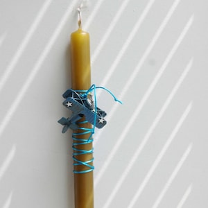 Può includere: Una candela gialla con una decorazione di aereo blu e un nastro blu avvolto intorno.