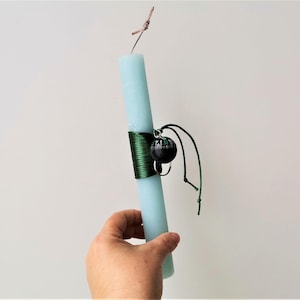 May include: A light blue candle with a green ribbon tied around it. A small black ornament hangs from the ribbon.
