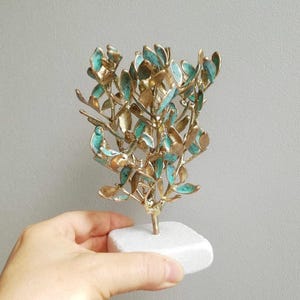 May include: A gold and turquoise metal sculpture of a small tree with a white marble base.