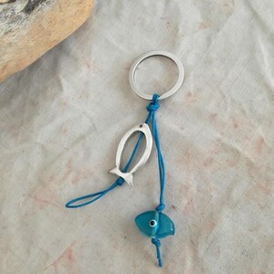 May include: A silver key chain with a blue glass fish charm and a silver fish charm. The charms are attached to a blue cord.
