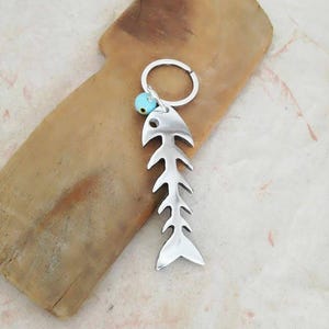 May include: Silver fish bone keychain with a turquoise blue bead.