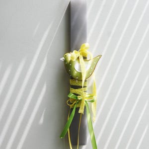 May include: A gray Easter candle decorated with yellow and green ribbon and a green bird with white polka dots.