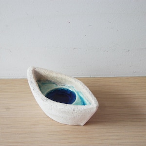 Peut inclure: Un plat en céramique blanche en forme de bateau avec un glaçage bleu et vert à l'intérieur.