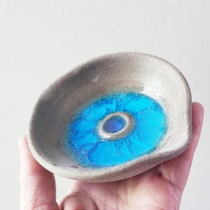 Peut inclure: Un petit plat en céramique gris avec un glaçage bleu et blanc. Le plat a un bord ondulé et un motif bleu et blanc au centre.