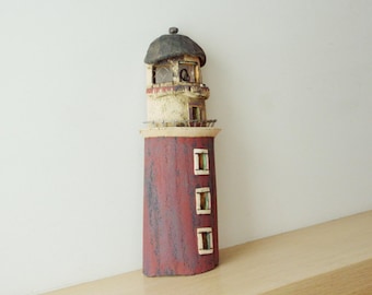 May include: A hand-crafted ceramic lighthouse figurine with a red and white exterior. The lighthouse has a black roof and three windows.