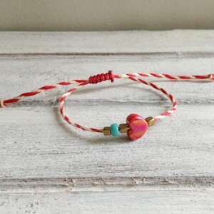 Op de afbeelding: Rood en wit touw armband met een rode hart charme en turquoise kralen.
