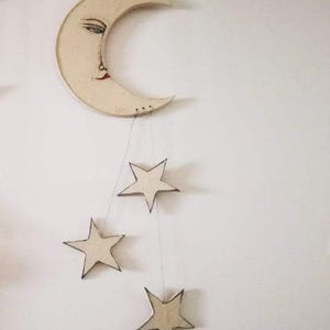 May include: A wooden crescent moon with a painted face hangs from the ceiling with three smaller wooden stars attached to it.