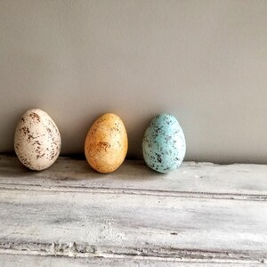 Pode incluir: Três ovos decorativos, um branco com manchas marrons, um amarelo com manchas marrons e um azul com manchas pretas.