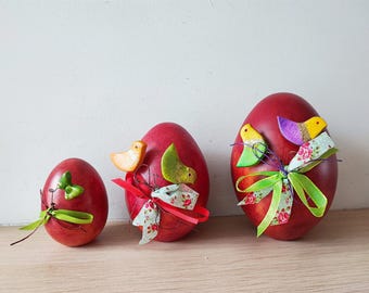 Op de afbeelding: Drie rode paaseieren versierd met kleurrijke vogels, linten en bloemenpatronen.
