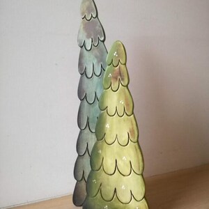 Peut inclure: Deux sapins de Noël en bois, l'un vert et l'autre bleu-vert, avec un design en couches et festonné. Les arbres sont posés sur une surface en bois.