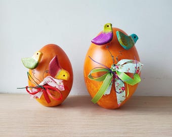 May include: Two orange Easter eggs decorated with colorful birds, ribbons, and floral fabric. The eggs are a popular spring decoration.