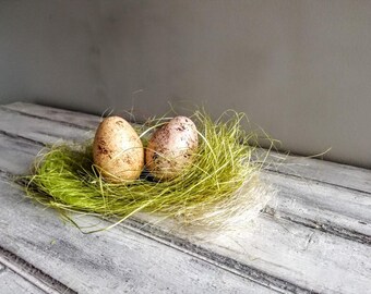 May include: Two speckled Easter eggs in a green and white nest made of shredded paper.