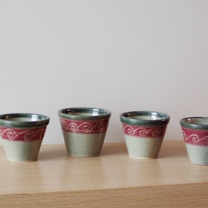 Könnte beinhalten: Vier kleine Keramikbecher mit einem grün-roten Design. Die Becher sind alle gleich groß und haben die gleiche Form, und sie haben ein schlichtes, elegantes Design.
