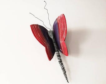 May include: A red and purple butterfly wall decor made from recycled materials. The butterfly has a wire body and antennae.