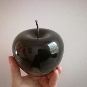 Puede incluir: Una manzana grande de cerámica negra y brillante con un tallo y una hoja.