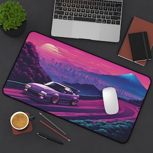 May include: A purple and pink gaming mouse pad with a retro-style illustration of a car driving on a winding road with a city skyline and a mountain in the background.