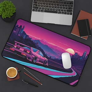 以下が含まれることがあります： ピンクとパープルのレトロなマウスパッド。街のスカイラインと、曲がりくねった道を走るピンクのスポーツカーが描かれています。マウスパッドには白いマウスが置かれています。