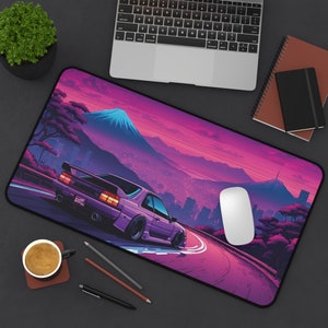 May include: A purple car drives on a winding road with a mountain in the background. The scene is set against a pink and purple sunset. The mousepad is designed with a retro aesthetic.