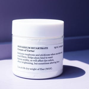 May include: A white jar of Potassium Bitartrate, also known as Cream of Tartar, with a white lid. The label provides instructions for use, including the weight of the product, 2.65 oz. The jar is on a purple surface.
