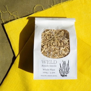 May include: A white paper bag with a clear window containing dried Weld Reseda luteola whole plant material. The label reads Weld, Reseda luteola, Whole Plant, 100g / 3.5oz, YELLOW, GREEN (IRON) and features a black botanical illustration.
