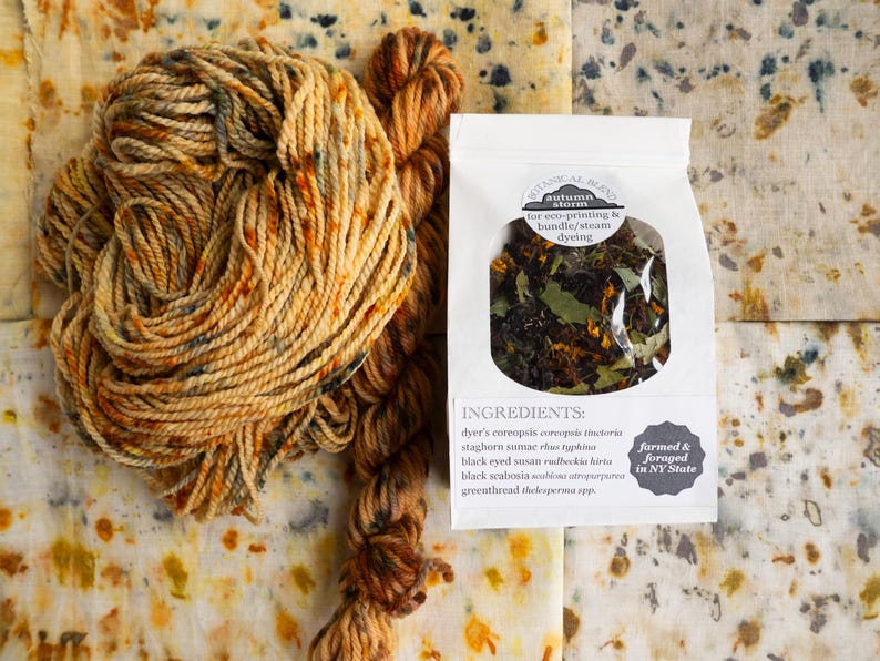 May include: A skein of variegated orange and brown yarn next to a white paper pouch labeled Botanical Blend Autumn Storm for eco-printing and bundle/steam dyeing, containing dried plant matter with a list of ingredients and farmed and foraged in NY State.