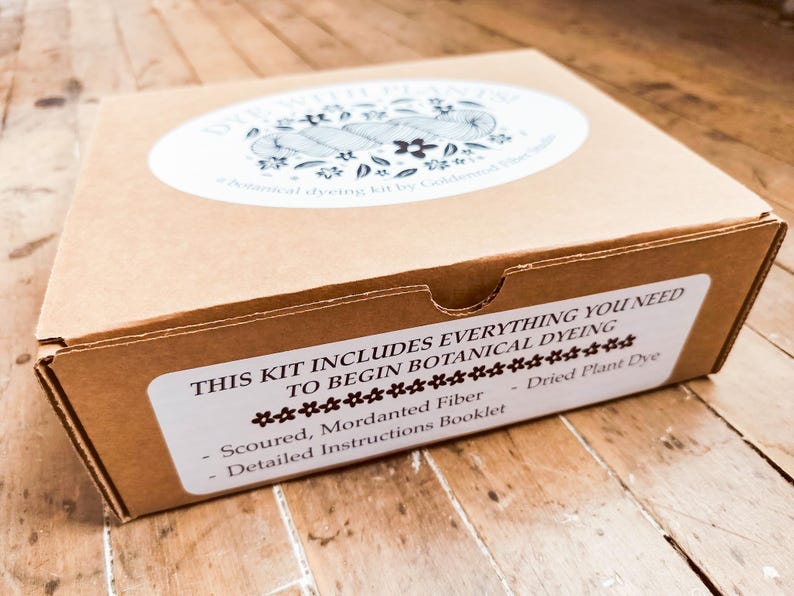 May include: A brown cardboard box for a botanical dyeing kit. The top label reads DYE WITH PLANTS! botanical dyeing kit by Goldenrod Fiber Studio. The front label reads THIS KIT INCLUDES EVERYTHING YOU NEED TO BEGIN BOTANICAL DYEING, Scoured, Mordanted Fiber, Dried Plant Dye, Detailed Instructions Booklet.