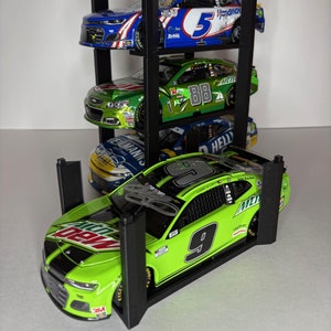 May include: A black metal display stand with four levels, holding four miniature race cars. The cars are green and blue with numbers 5, 88, and 9. The top car is blue with the number 5 and the word "Hendrick" on the side. The bottom car is green with the number 9 and the words "Mountain Dew" and "3M" on the side.