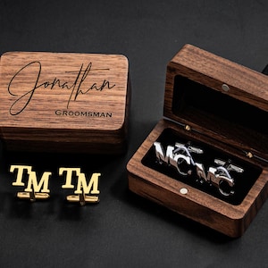 May include: A wooden box with a hinged lid, engraved with the name "Jonathan" and the word "Groomsman". The box contains a pair of silver cufflinks with the initials "TM" engraved on them.