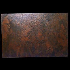 May include: A close-up of a copper metal sheet with a textured, mottled surface. The metal has a dark brown and reddish-brown colour with a subtle sheen.