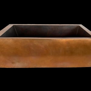 May include: A large, rectangular copper sink with a hammered finish. The sink is empty and has a dark brown interior.