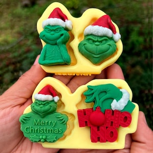 May include: A set of four green Grinch-themed molds with red Santa hats and white trim. One mold has the text "Merry Christmas" and another has "HO HO HO". The molds are in a yellow tray.