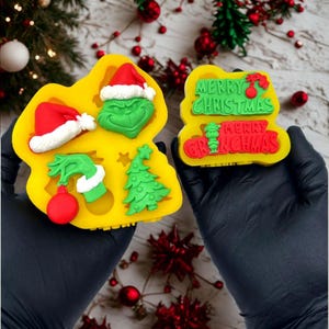 May include: Two yellow silicone molds with Christmas-themed designs. One mold features a Grinch face, Santa hat, Christmas tree, and a hand holding an ornament. The other mold says "Merry Christmas" and "Merry Grinchmas".