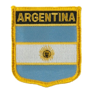 May include: A shield-shaped embroidered patch featuring the flag of Argentina with light blue and white horizontal stripes and a central yellow sun emblem. The word ARGENTINA is stitched in yellow letters on a black background at the top.