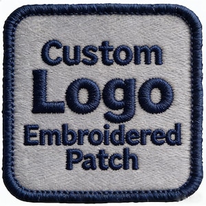 Puede incluir: Un parche bordado de forma cuadrada con un fondo gris claro similar al fieltro y un borde cosido en azul marino oscuro. El texto "Custom Logo Embroidered Patch" está bordado con hilo azul marino oscuro en el centro del parche.