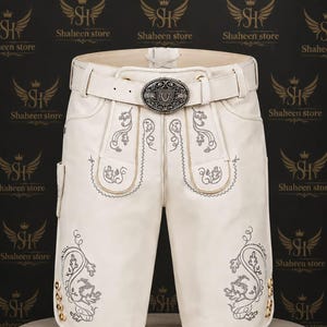 Könnte beinhalten: Cremefarbene Lederhose mit dekorativer Stickerei und passendem Gürtel. Die Hose hat eine silberne Schnalle und goldfarbene Knöpfe. Der Hintergrund enthält den Text "Shaheen store".