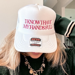 Puede incluir: Gorra de camionero blanca con texto bordado en rojo que dice "Sé que tengo las manos llenas". La gorra tiene una etiqueta negra con texto blanco que dice "Otto World Famous Foam Front OSPM Trucker Durable Snap Closure".