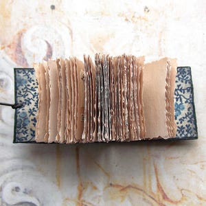 May include: A small, handmade book with pages made of thin, textured paper. The book is bound in a dark blue fabric with a floral pattern.