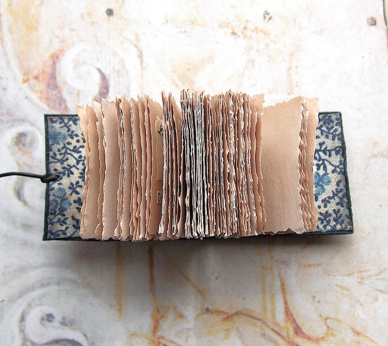 May include: A small, handmade book with pages made of thin, textured paper. The book is bound in a dark blue fabric with a floral pattern.