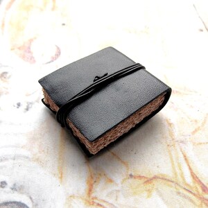 May include: A small black leather-bound journal with a brown paper cover and a black string closure.