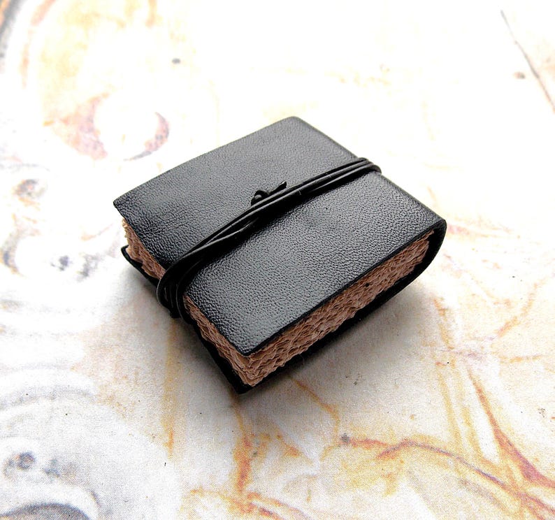 May include: A small black leather-bound journal with a brown paper cover and a black string closure.