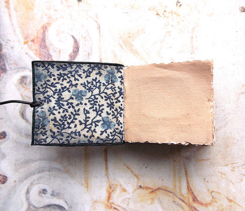 May include: A small, handmade notebook with a blue and white floral patterned cover and a blank, brown paper interior.