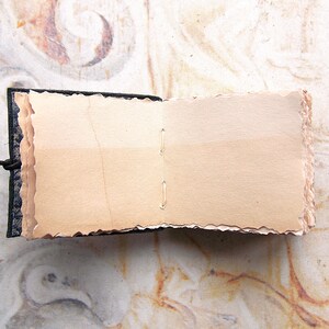 May include: A small, handmade book with a black fabric cover and blank, cream-colored pages. The pages have a rough, textured edge.